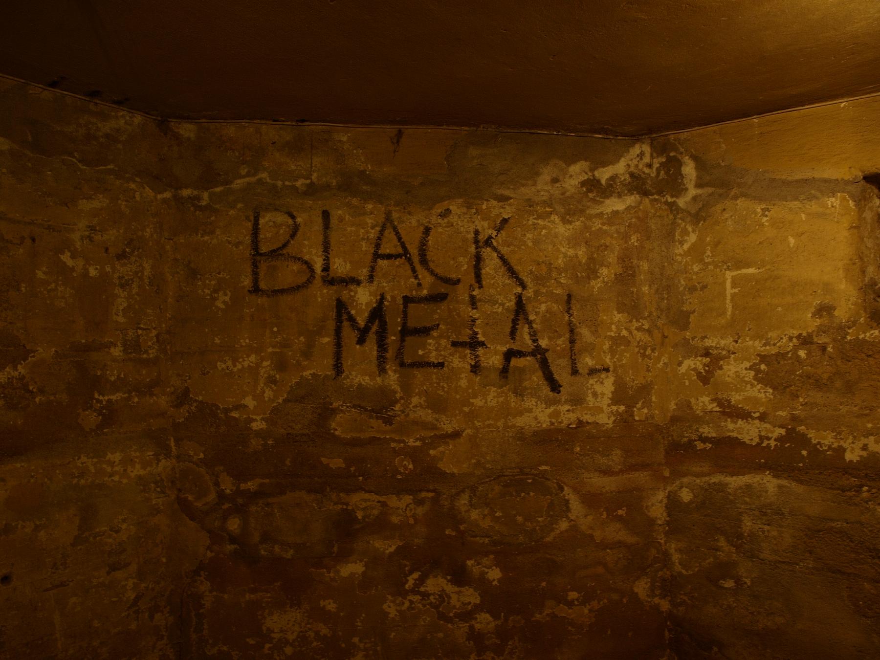 a man in a room with graffiti on the wall - File:Helvete Oslo - black metal graffiti.jpg